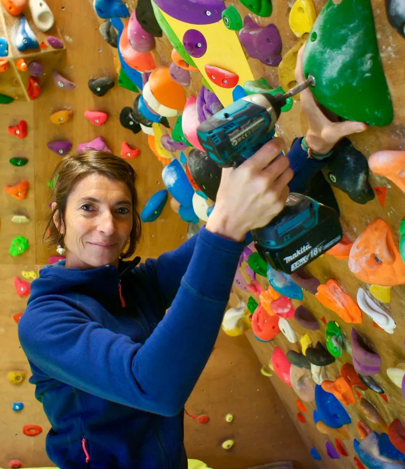 Chloé visse une prise sur un mur de blocs couvert de prises de couleur